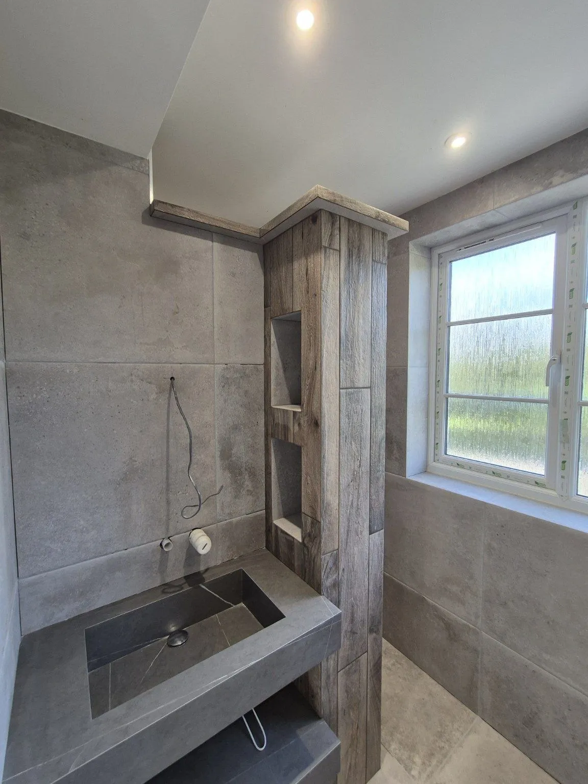 Bespoke wood-effect tiled partition with recessed niches and precision-mitred projecting bulkhead in a contemporary bathroom